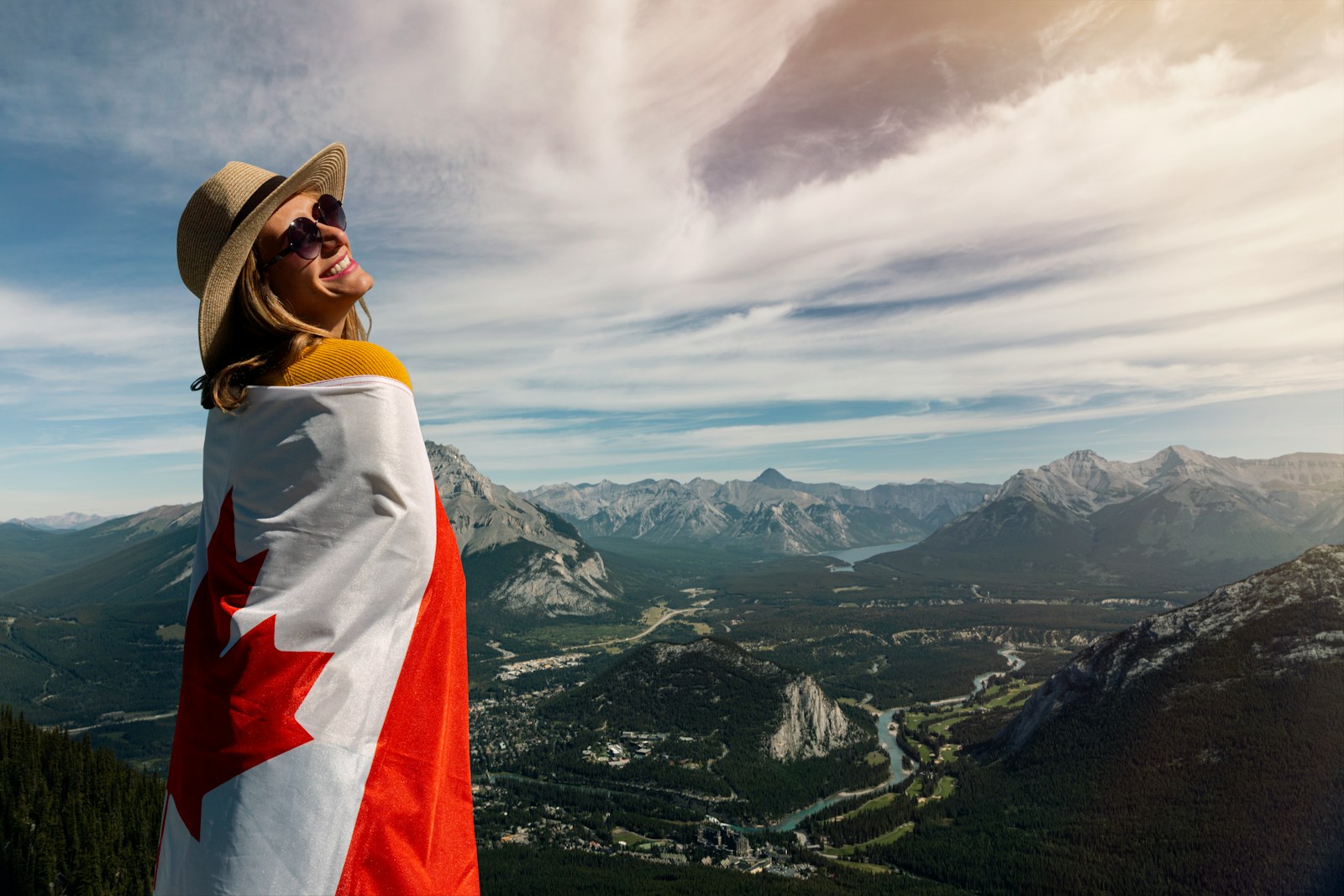smiling woman wearing brown hat and sunglasses while holding Canada flag